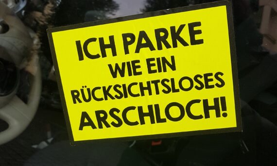 Bild eines Stickers mit dem Satz "Ich parke wie ein rücksichtsloses Arschloch" an einer Autoscheibe
